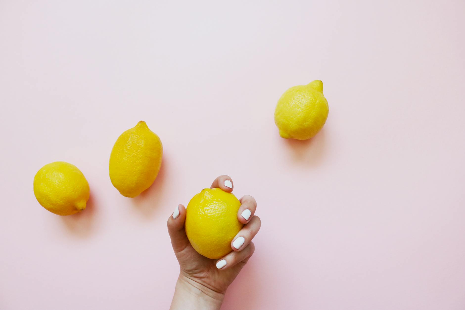 Hand holding fresh lemon on soft pink background with lemons nearby