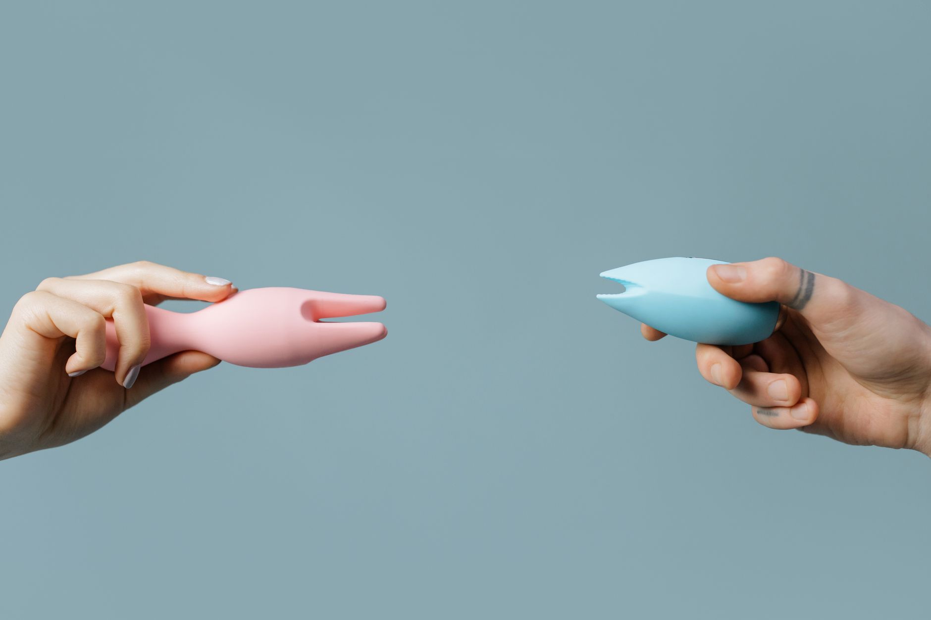 Two hands holding complementary vibrators, representing couples collaboration and shared pleasure.