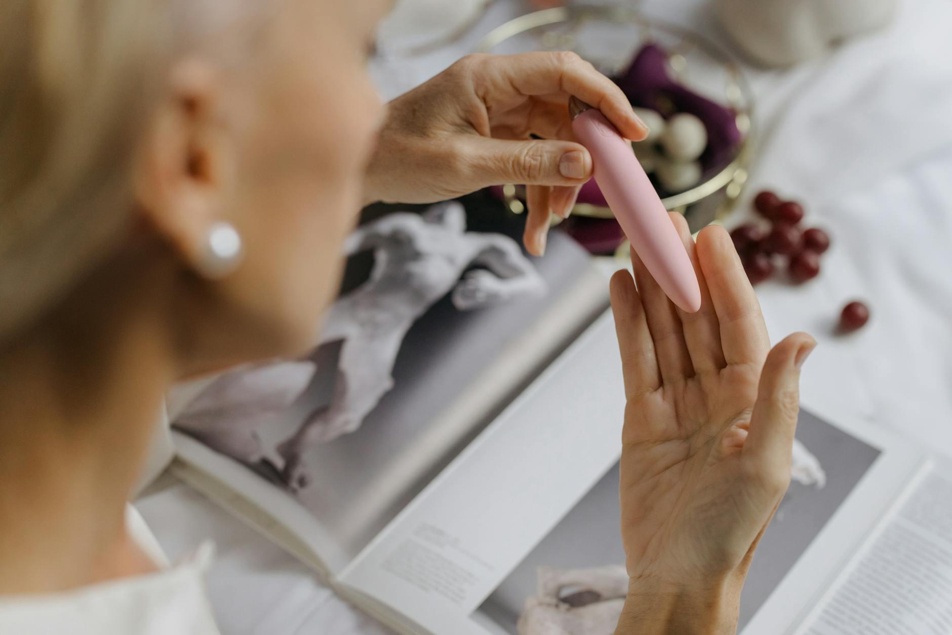 A close-up of someone holding a pink vibrator near personal items, symbolizing intimate pleasure after physical recovery.