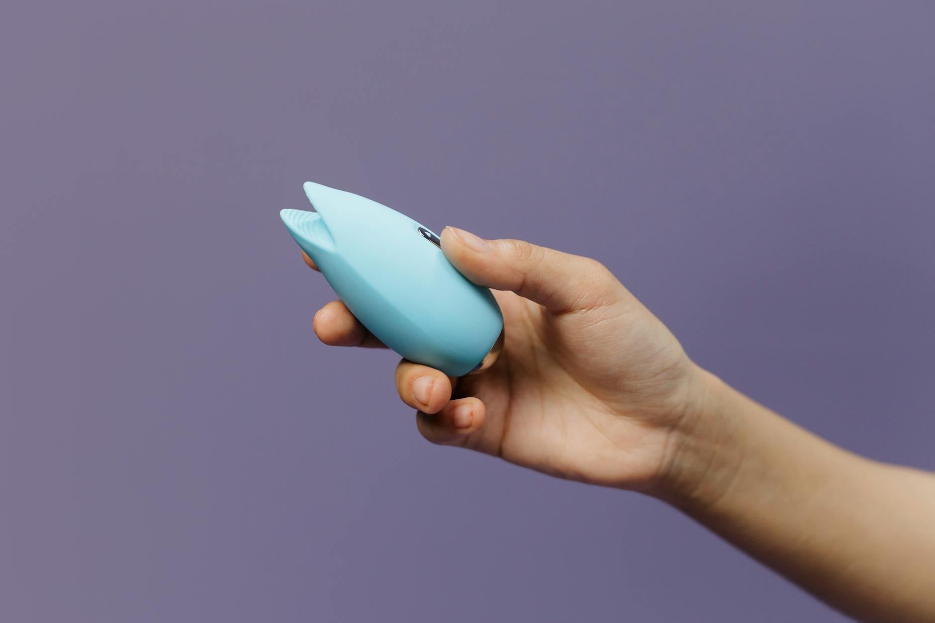A hand holding a silicone clitoral vibrator against a purple background, showcasing sexual wellness and pleasure