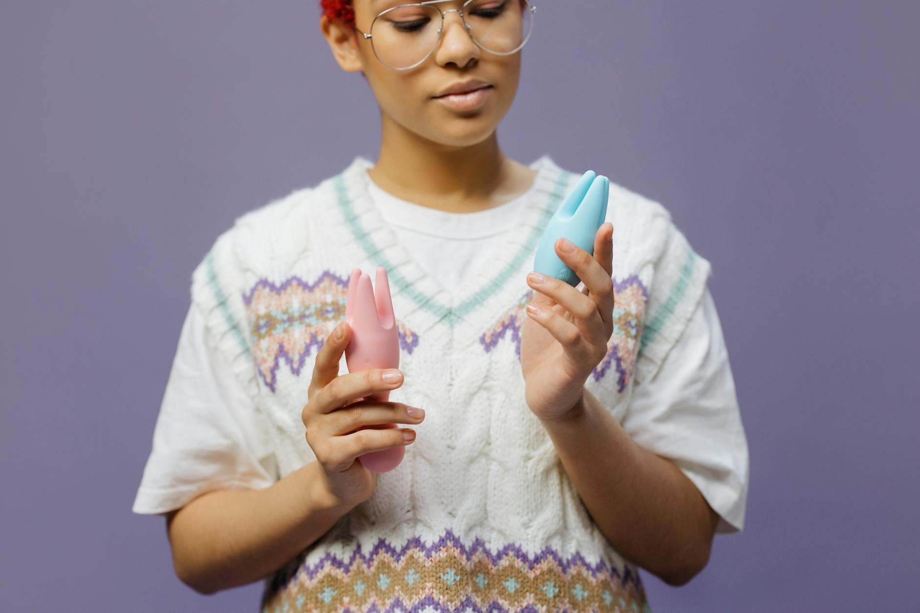 Woman holding blue and pink silicone vibrators in a contemplative pose, representing solo pleasure exploration.